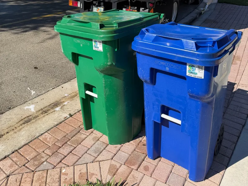 Freshly cleaned green trash can and blue recycling can back at the curb with Bin There Clean That stickers