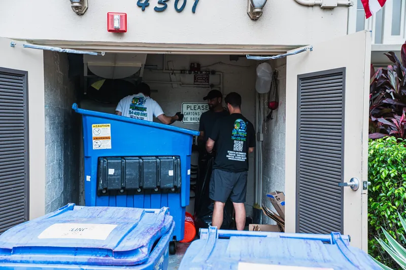 Crew members cleaning inside a building dumpster enclosure