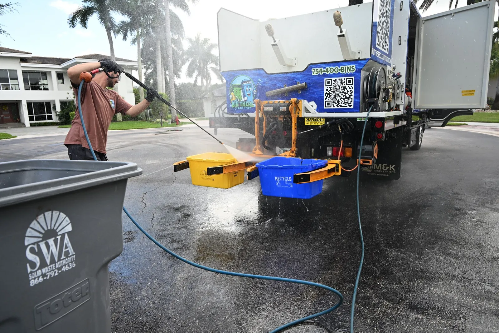 Bin There Clean That crew member pressure washing trash bins at the truck