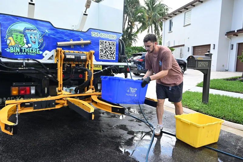 Crew member placing a blue recycling bin on the truck lift