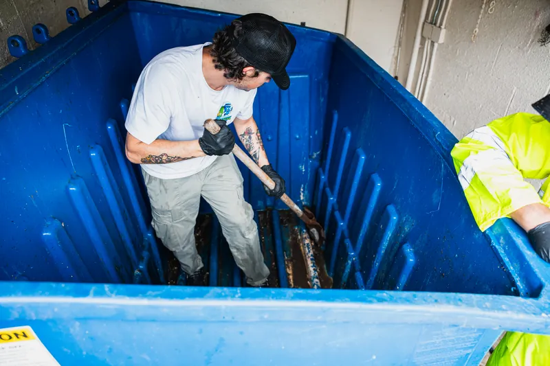Technician scrubbing the inside of a dumpster